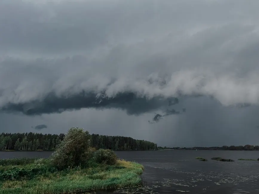 A powerful storm cloud formation looms over a tranquil lake and forest, capturing nature's dynamic beauty.